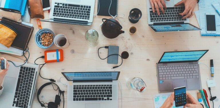An image of computers on a table with some hand visible working on them